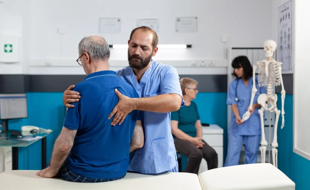 Chiropractor treating retired patient with back pain in hospital.