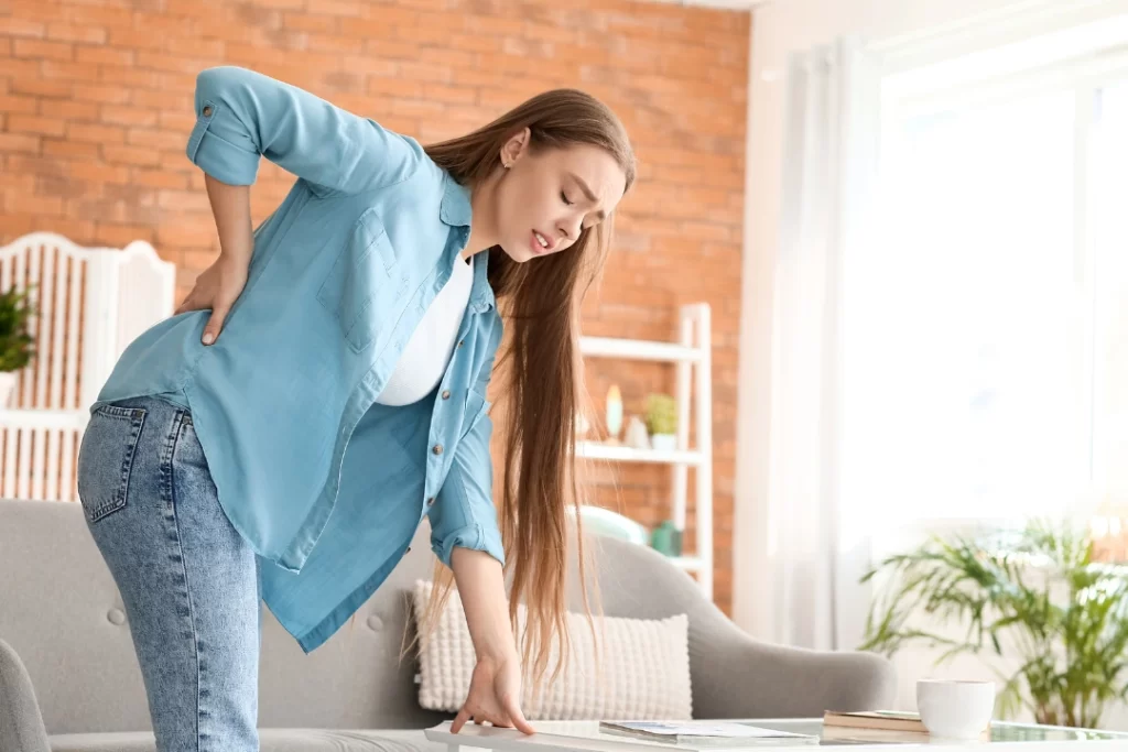 Young girl is holding her lower back, while standing and suffering from unbearable pain.