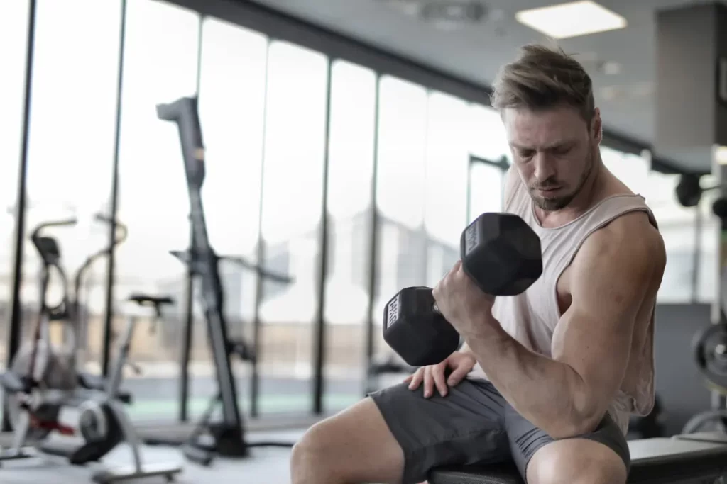 Man in White Tank Top and Grey Shorts Lifting Dumbbell.