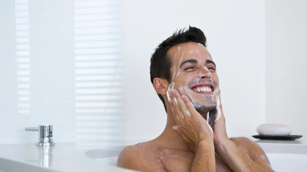 man applying facial cleanser on his face 